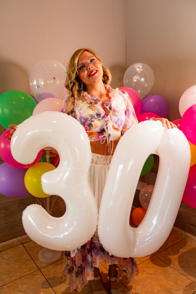 Portrait festif d’une femme célébrant ses 30 ans entourée de ballons, photographie d’événement privé joyeuse et colorée.