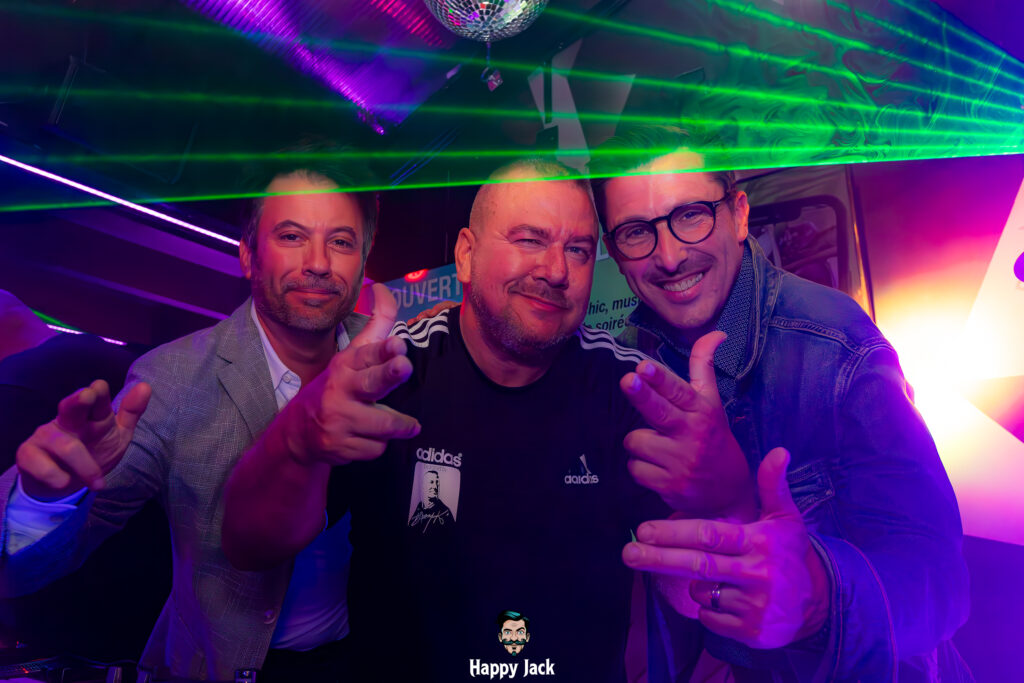 Le DJ Daddy K entouré de clubbeurs les bras levés sous les lasers violets lors d'un événement clubbing.