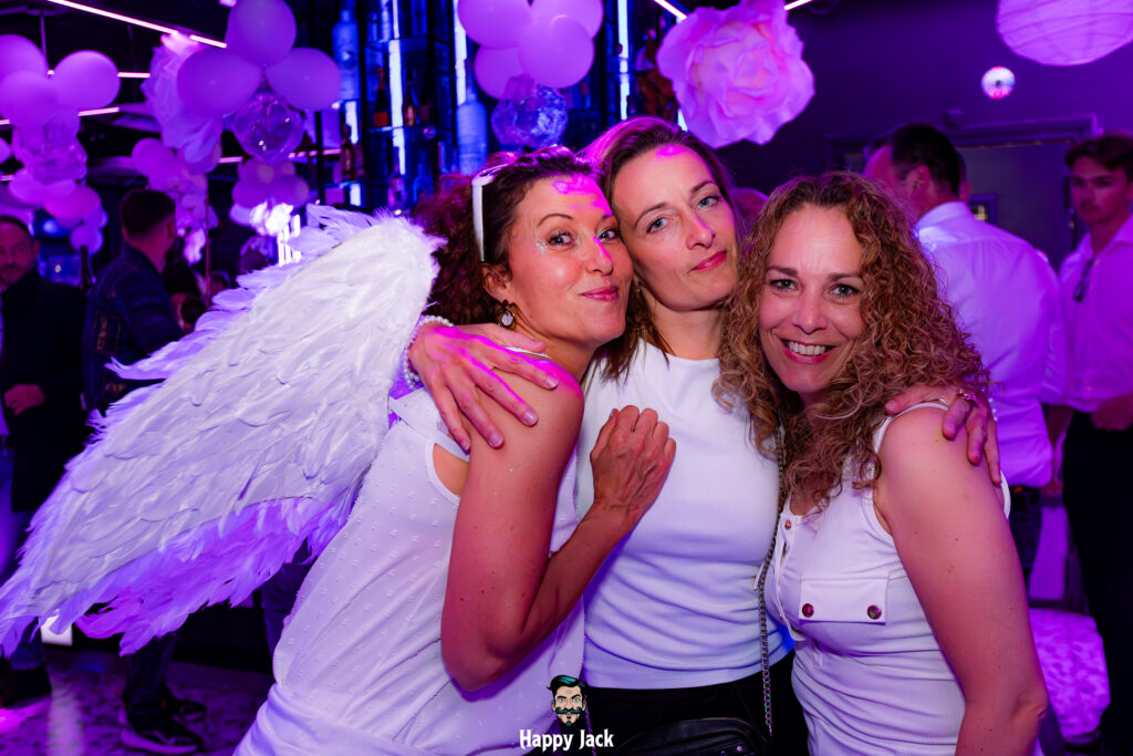 Trois jeunes femmes en tenue blanche avec des ailes d'ange lors d'une soirée à thème clubbing.