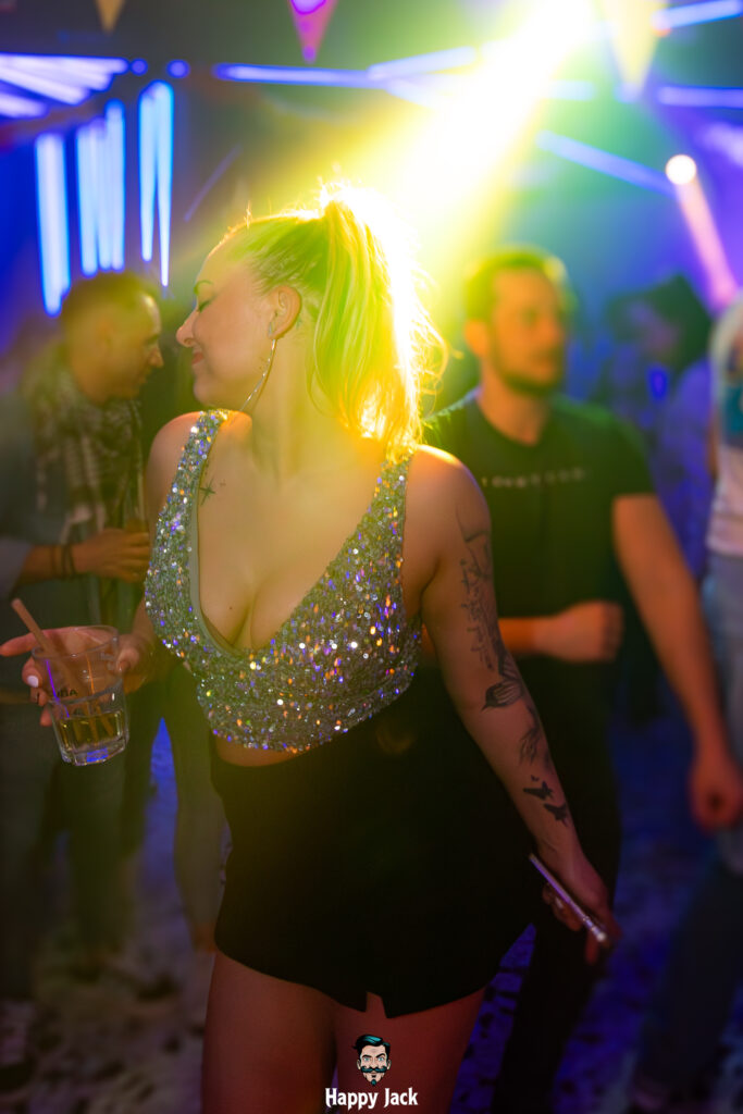 Jeune femme aux paillettes dansant les yeux fermés sous un projecteur jaune intense sur le dancefloor.