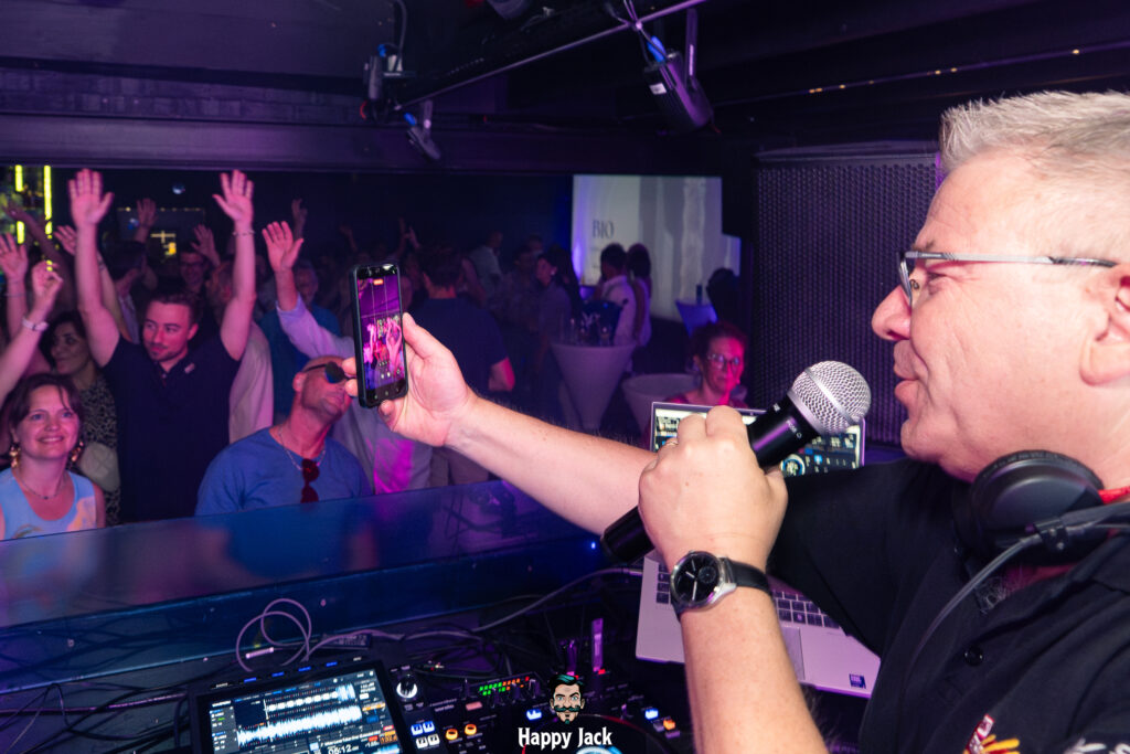 DJ au micro filmant le public avec son smartphone pour ses réseaux sociaux en plein set de house music.
