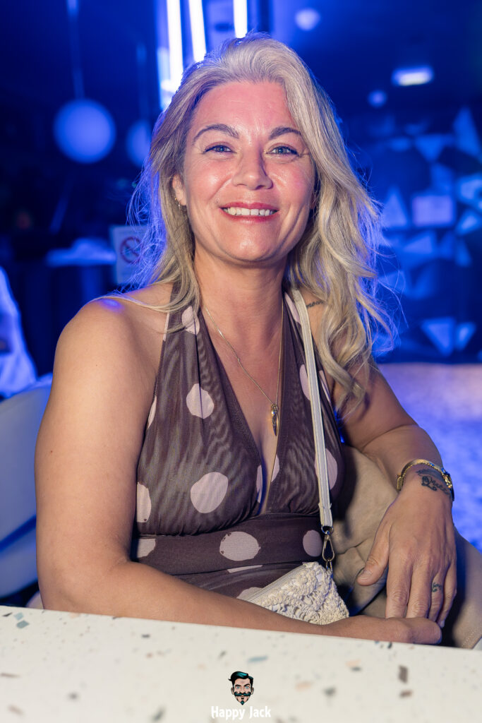 Portrait d'une femme souriante assise à table en fin de soirée de musique électronique.